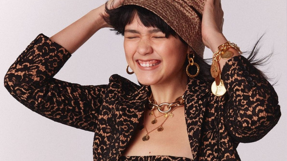 Smiling model wearing Ben-Amun gold jewelry and hat