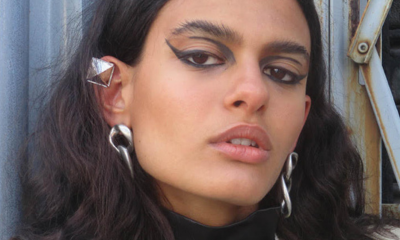 Model with graphic black eyeliner staring into camera, wearing silver chainlink earrings and a diamond-shaped silver ear-cuff