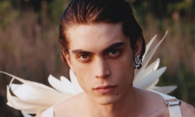 Male model clos-up of face and white wings worn on back, with one crystal and pearl earring