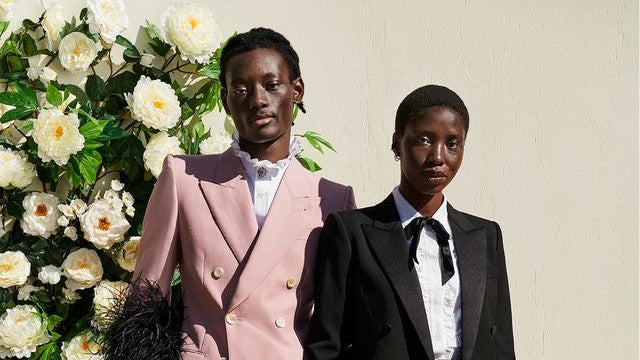 2 models pose in suits next to flowers for Harper's Bazaar