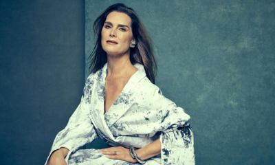 Brooke Shields posing against gray background in white patterned dress and silver jewelry