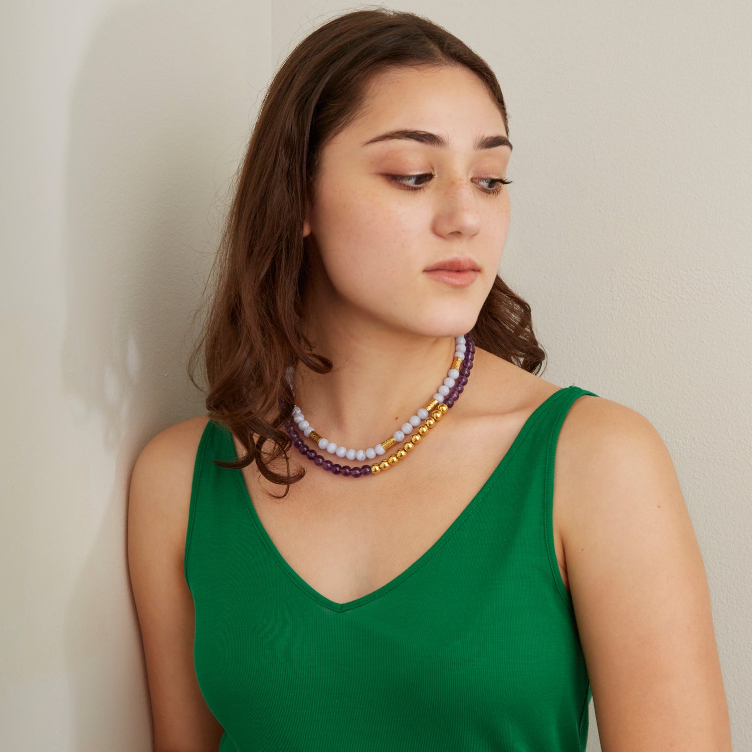 woman in green top wearing light and dark purple stone necklaces with gold beads