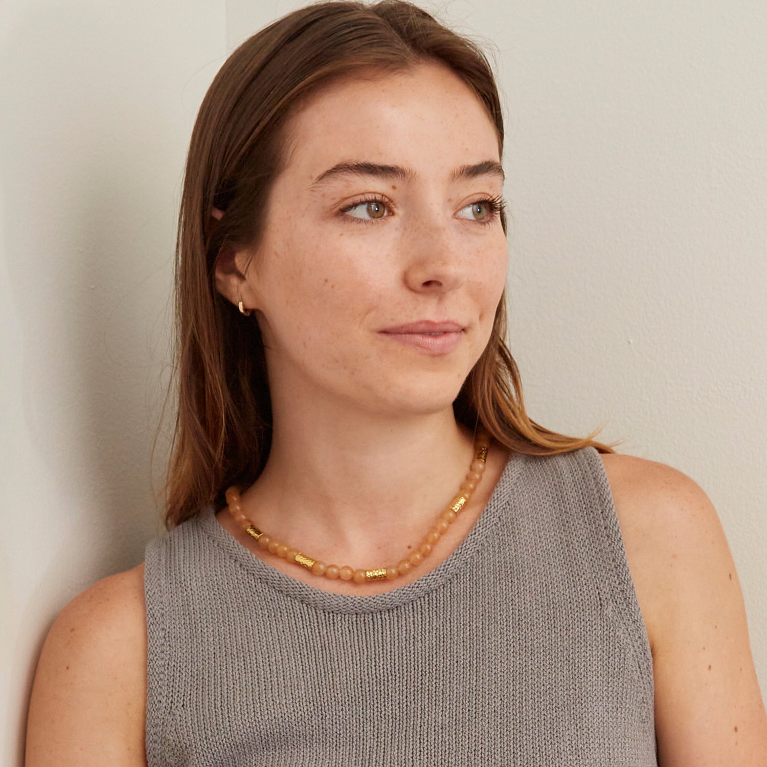 woman in gray tank top wearing orang stone necklace with gold beads