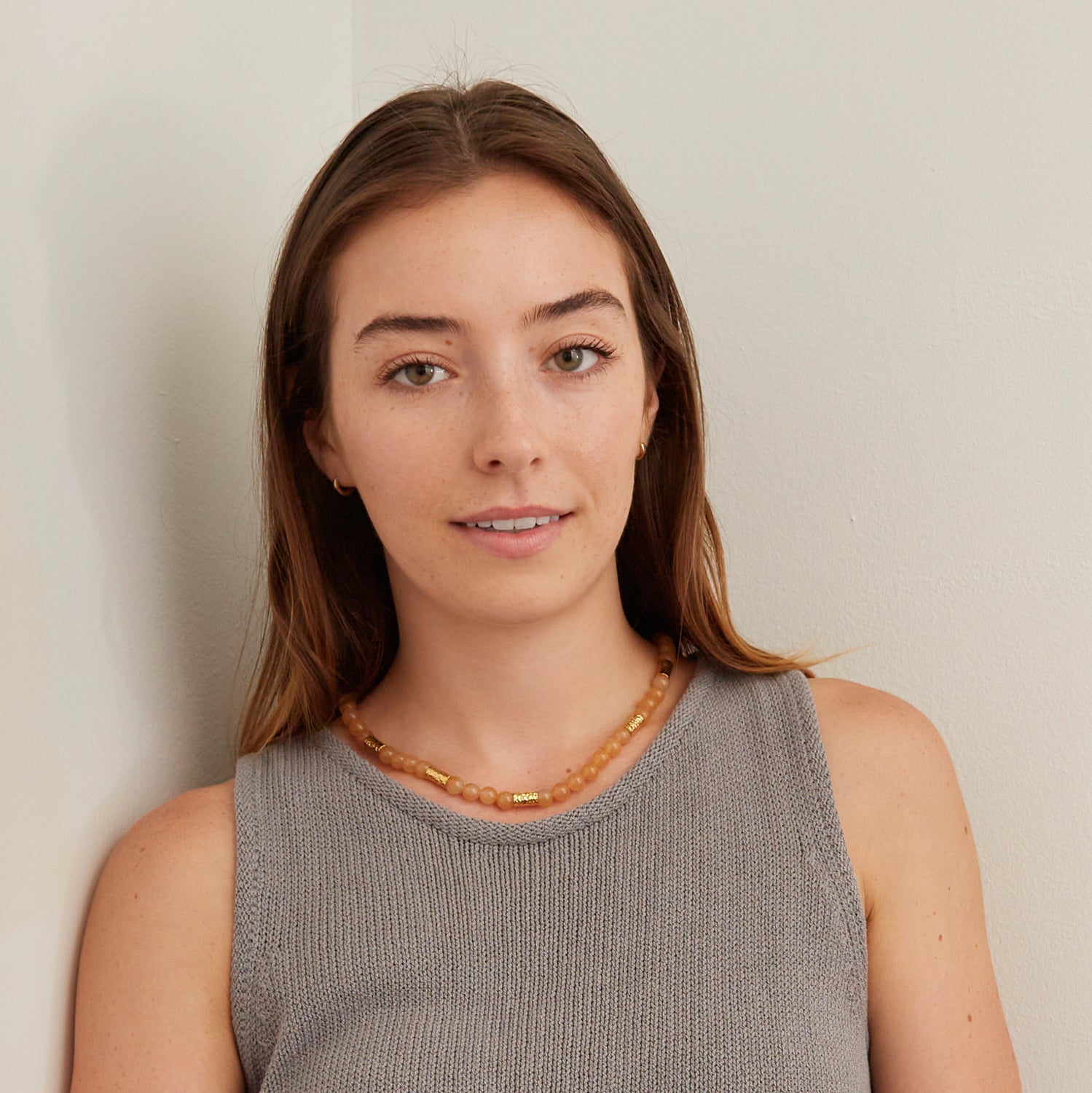 woman in gray tank top wearing orang stone necklace with gold beads