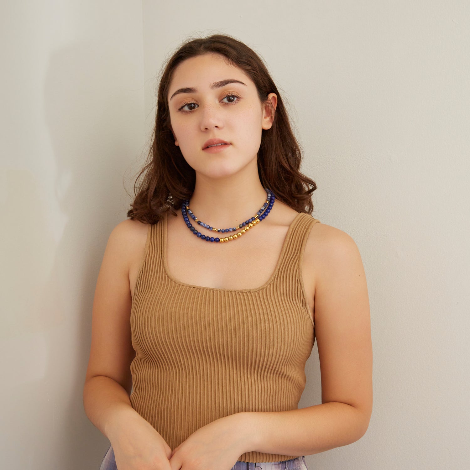woman in tan tank top wearing two blue necklaces with gold beads