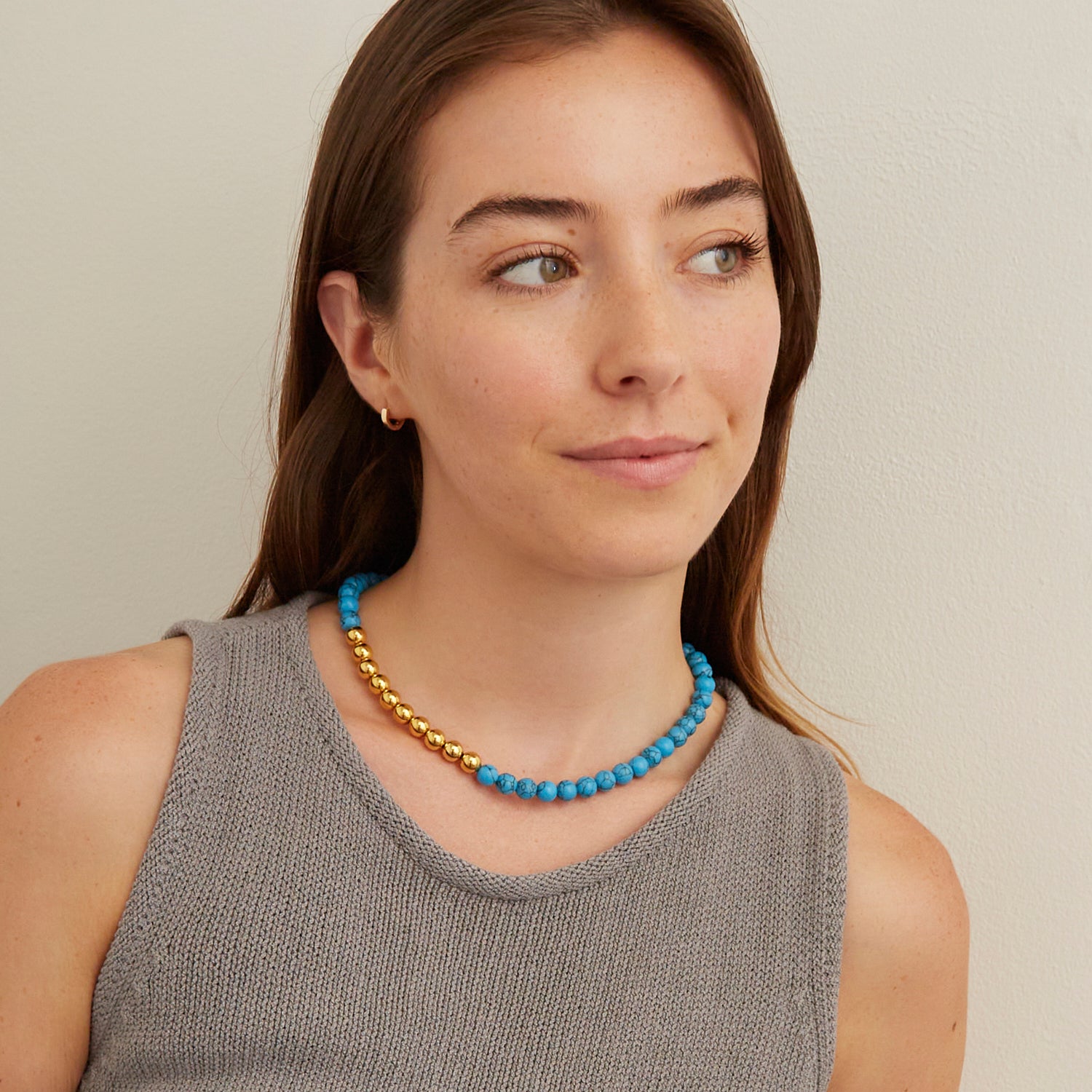 woman in gray vest wearing cyan blue marble stone necklace with gold beads