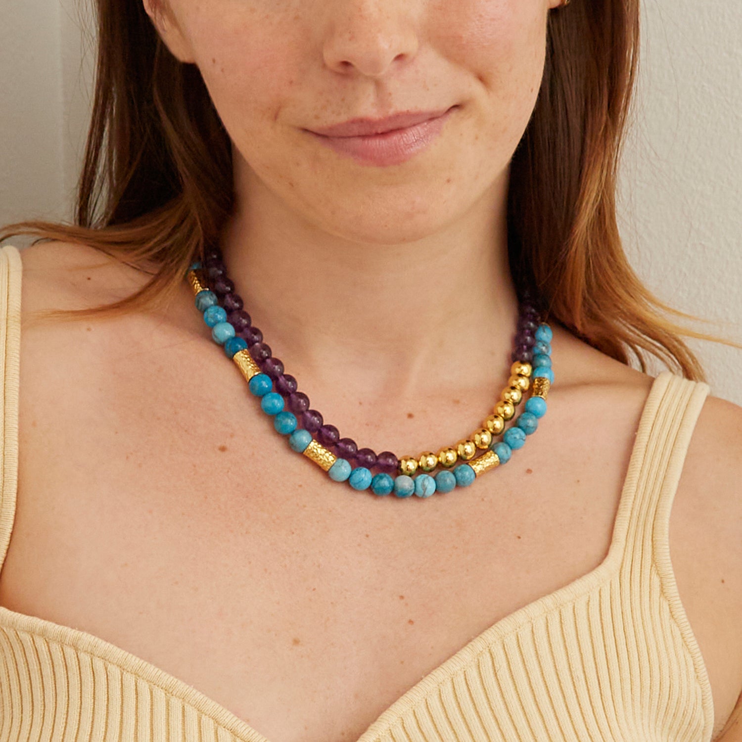 woman in tan tank top wearing purple and blue stone necklaces with gold beads