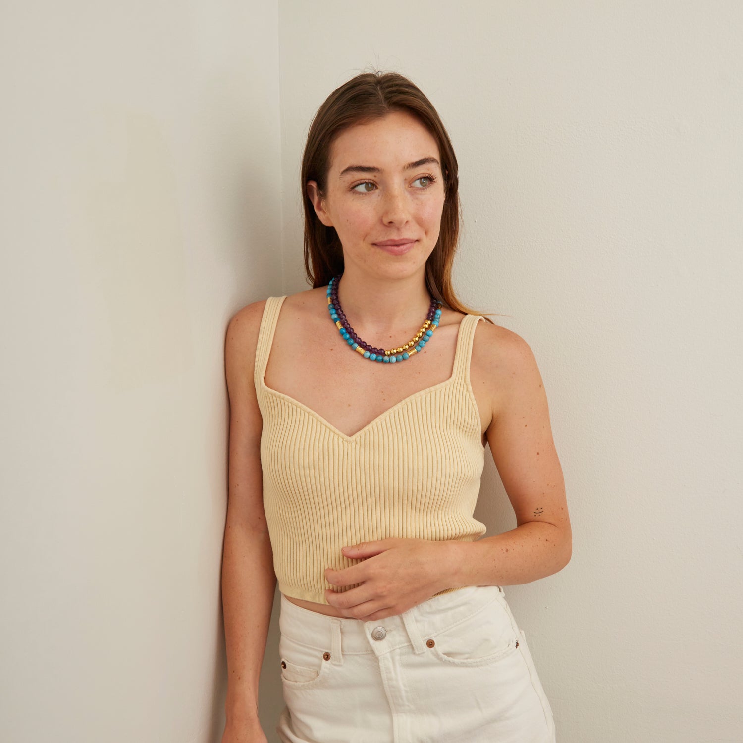 woman in tan tank top wearing purple and blue stone necklaces with gold beads