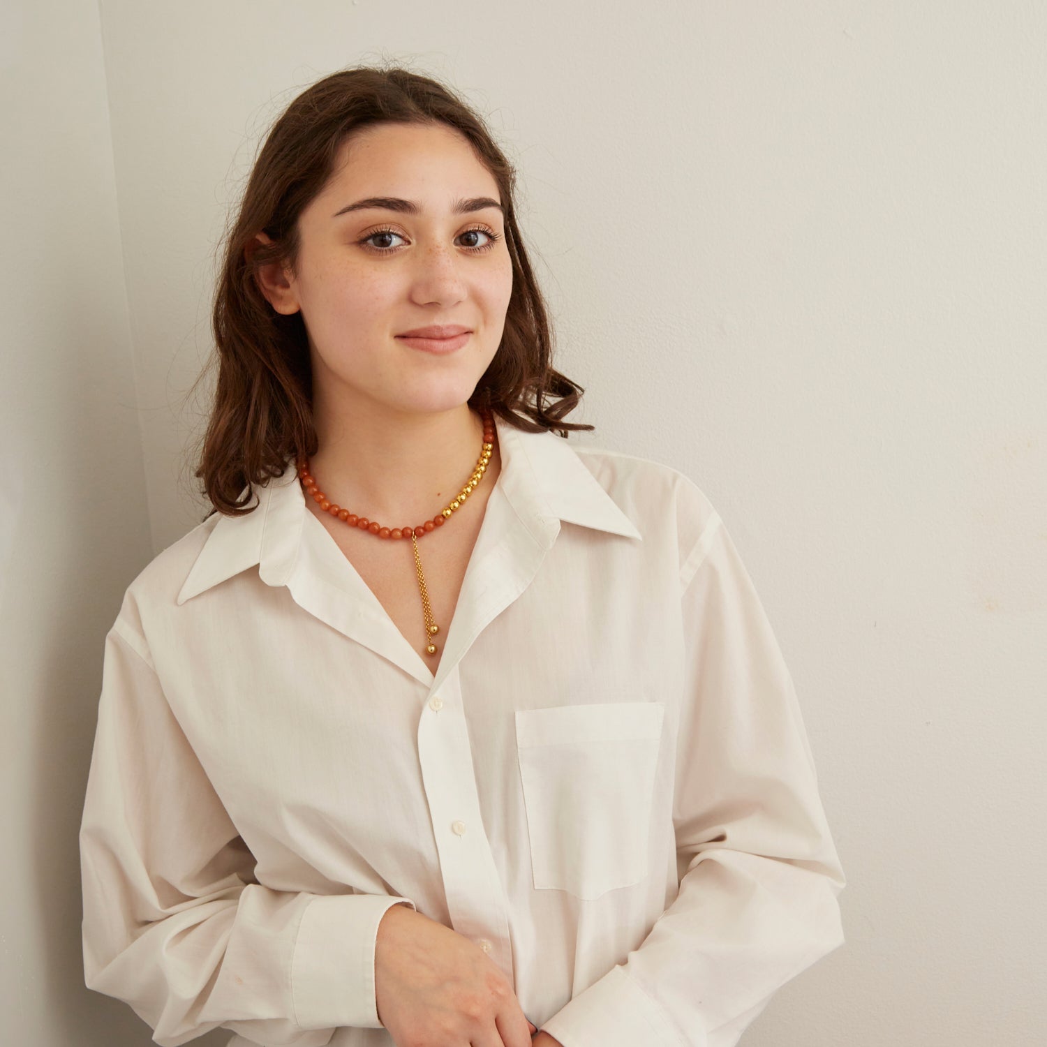 woman wearing white collared shirt and tangerine orange stone necklace with gold beads and hanging chain