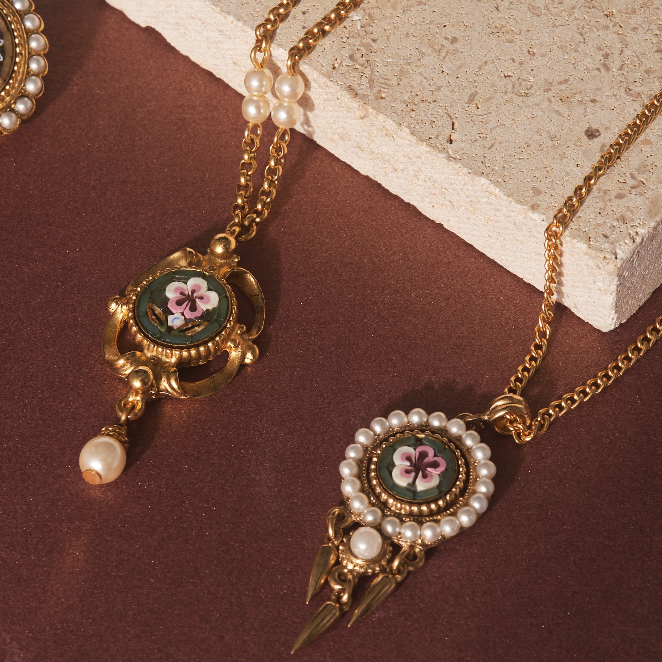 Flatlay of two Ben-Amun necklaces against stone and maroon background 
