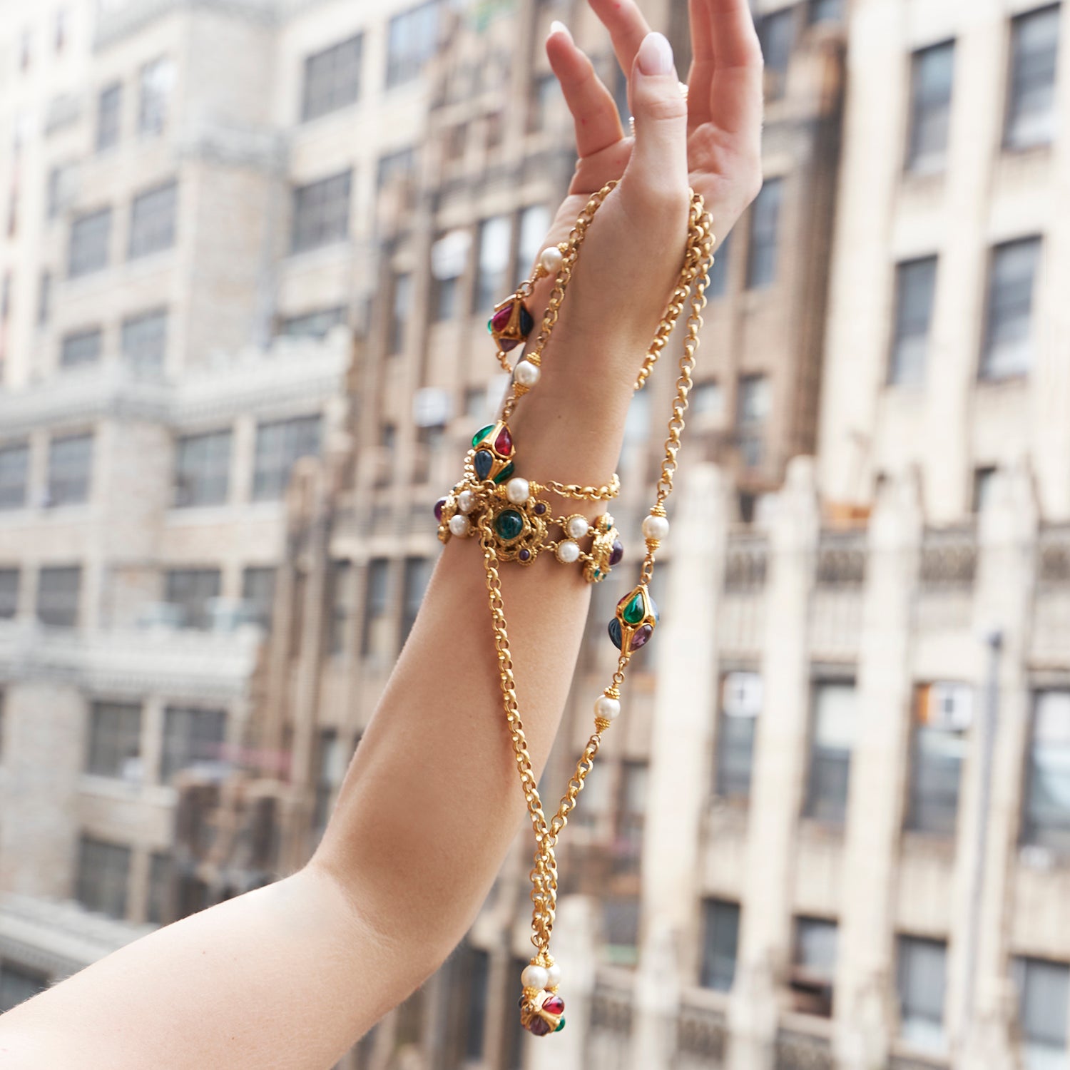 Hand holding gold necklace with green, red, and blue czech glass stones and majorca pearls