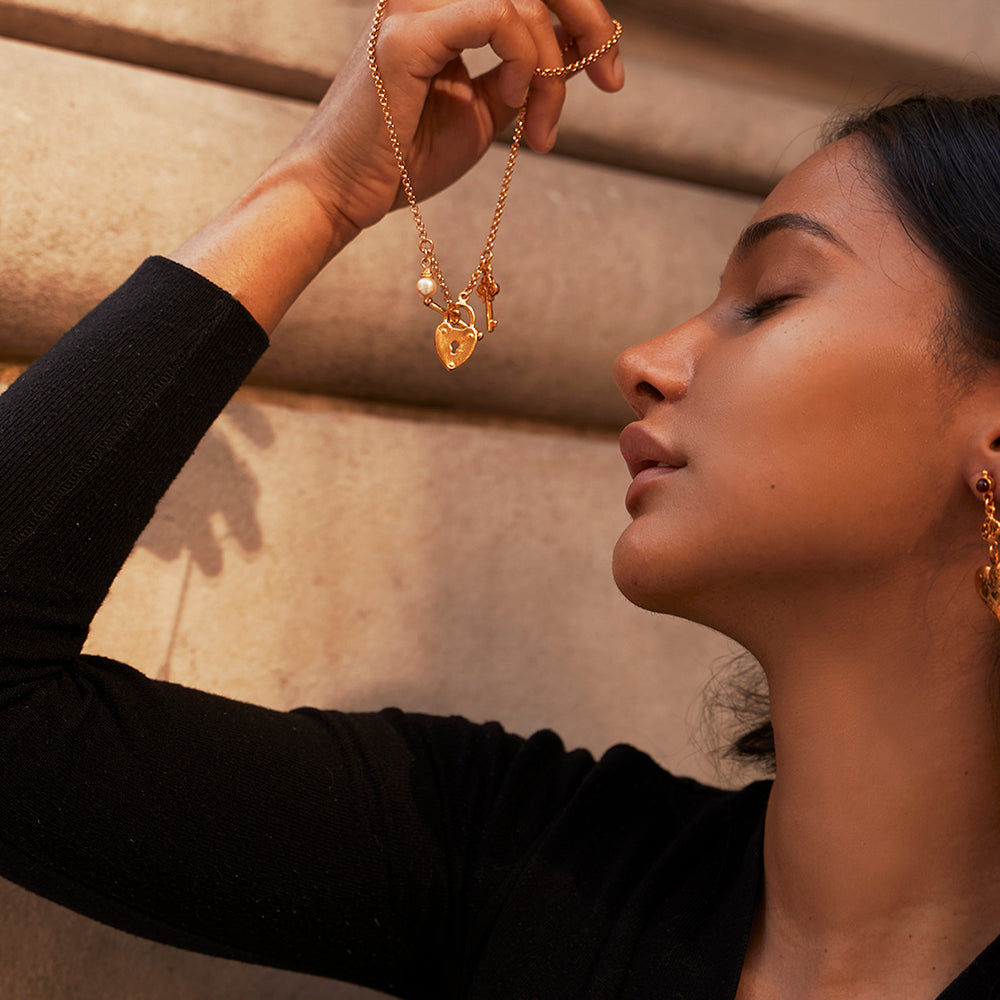model holding gold chain with pearl, locket, and key charms