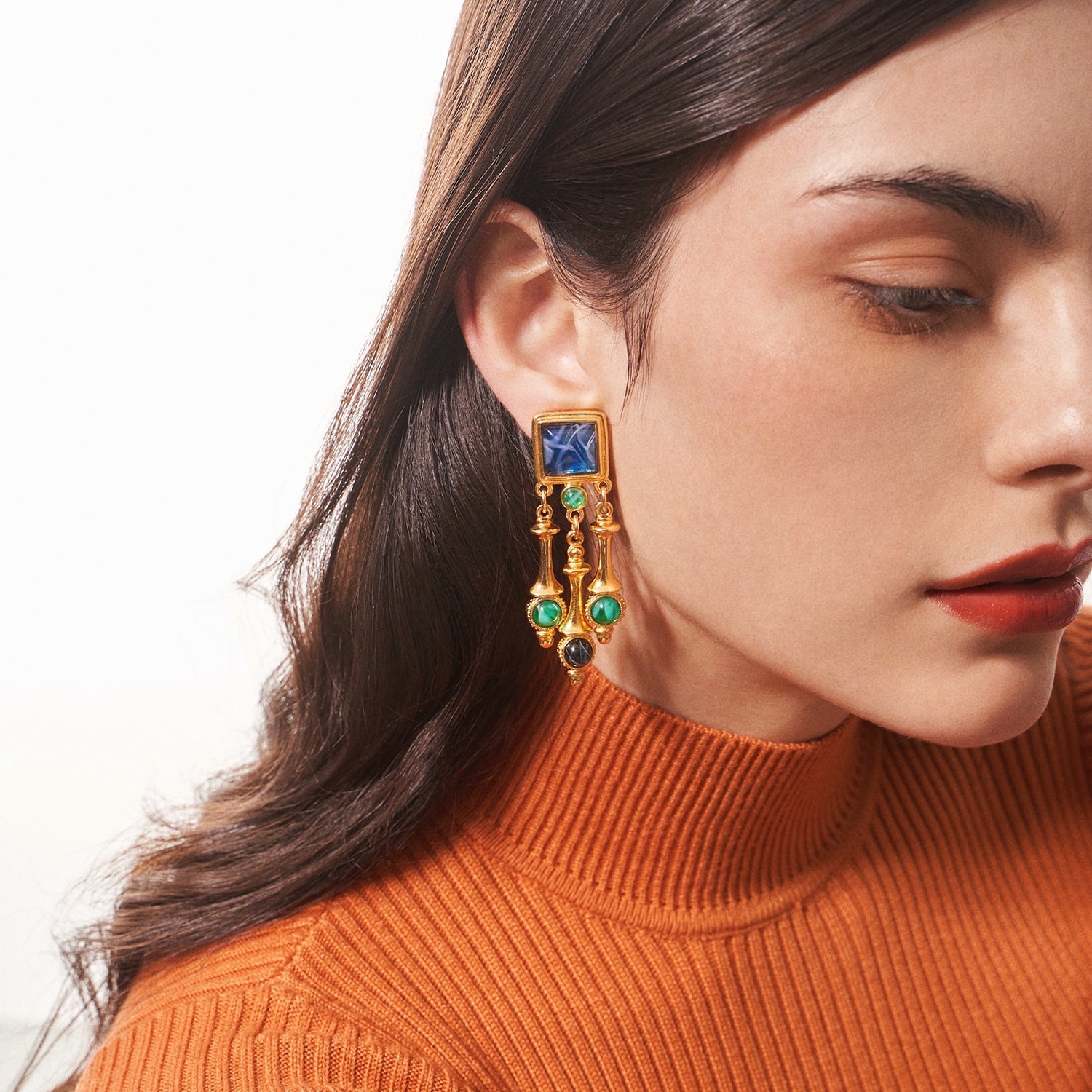 model wearing ben amun lucresia collection gold clip-on earrings inlayed with blue, green, and purple stones 